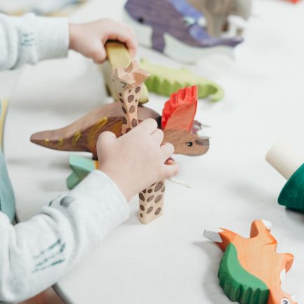 child holding brown and green wooden animal toys