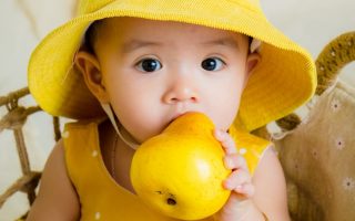 toddler in yellow top and hat holding fruit